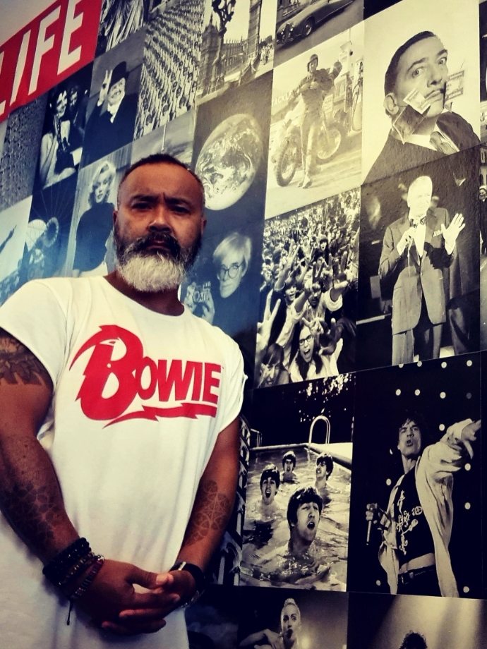 Donald, de man achter Headz for Hair, in een Bowie-shirt voor een wand met iconische zwart-witfoto's