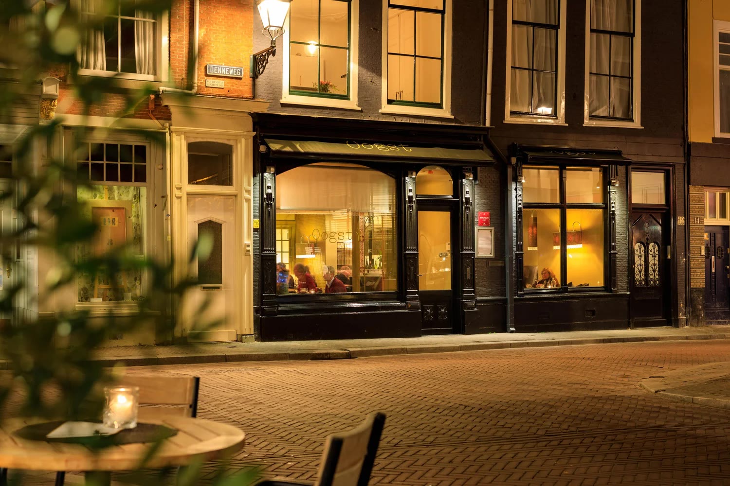 De verlichte gevel van Restaurant Oogst aan de Denneweg bij avond