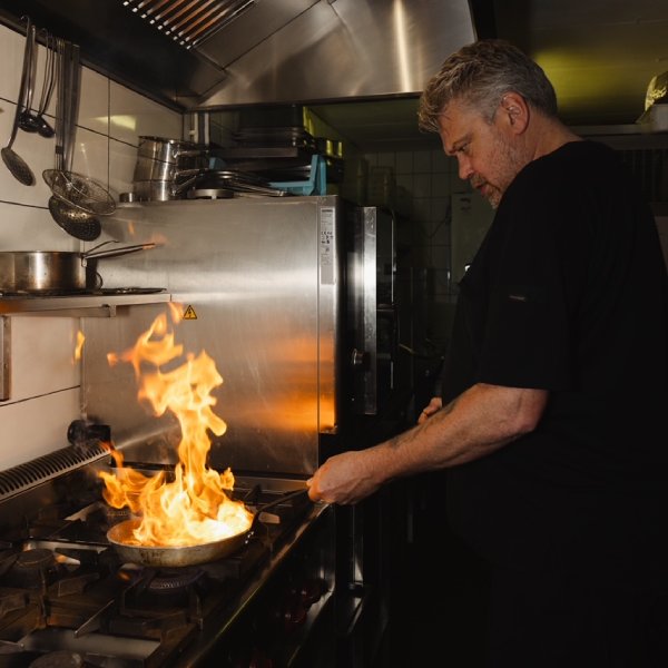 De chef in de keuken, met vlammen in de pan