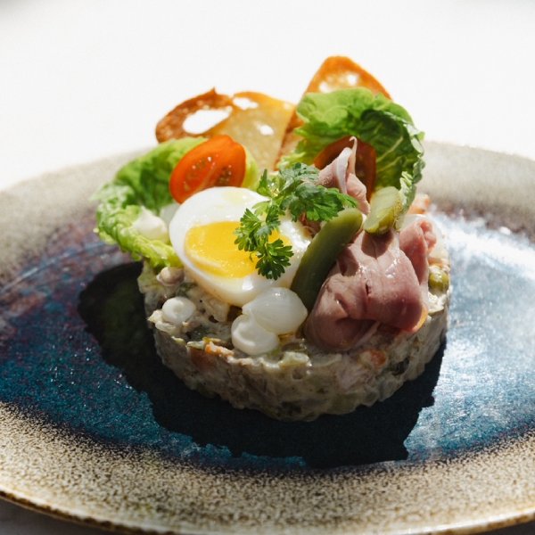 Verfijnd gerecht met ei, rosbief en groene salade op een blauw bord
